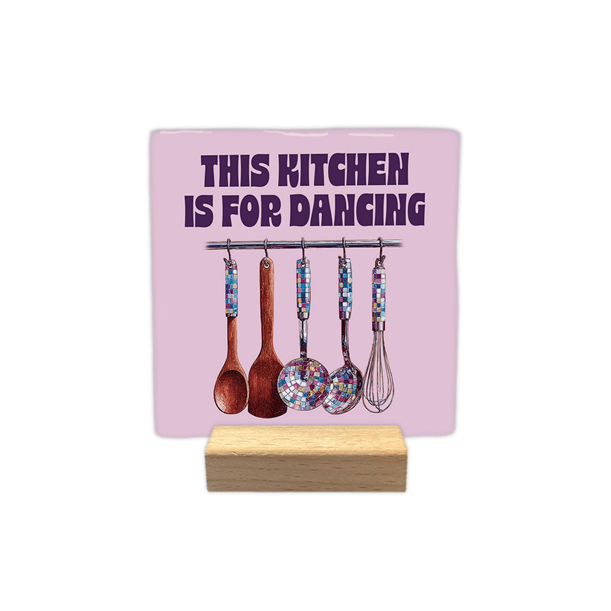 This kitchen is for dancing - Decoratie tegel - Formaat: - Op deze decoratie tegel staat een illustratie van vijf keukengerei-items die aan een metalen stang hangen tegen een roze achtergrond. Sommige items hebben handvatten of delen die lijken op een discobal met kleurrijke mozaïektegeltjes. Bovenaan de afbeelding staat in grote, donkerpaarse letters de tekst "THIS KITCHEN IS FOR DANCING". - Snelwenskaart