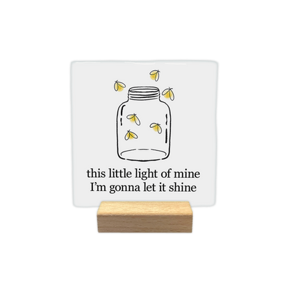 This little light - Decoratie tegel - Formaat: - Op deze decoratie tegel staat een getekende glazen pot met daarin en eromheen kleine, oplichtende vuurvliegjes. Onderaan staat in zwarte letters de tekst "this little light of mine, I'm gonna let it shine". De afbeelding is geplaatst op een witte achtergrond. - Snelwenskaart