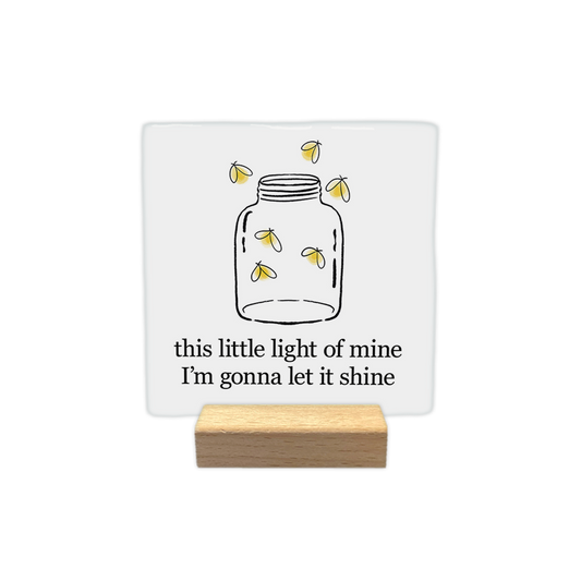 This little light - Decoratie tegel - Formaat: - Op deze decoratie tegel staat een getekende glazen pot met daarin en eromheen kleine, oplichtende vuurvliegjes. Onderaan staat in zwarte letters de tekst "this little light of mine, I'm gonna let it shine". De afbeelding is geplaatst op een witte achtergrond. - Snelwenskaart