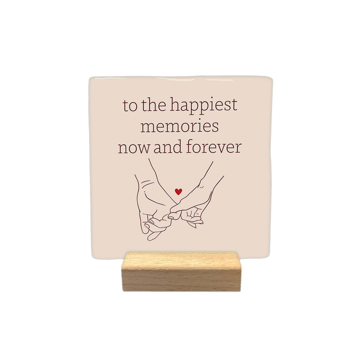To the happiest memories now and forever - Decoratie tegel - Formaat: - Op deze decoratietegel staat de tekst "to the happiest memories now and forever" in bruine letters, gecentreerd boven een lijntekening van twee handen die elkaars pink vasthouden. Tussen de handen is een klein, rood hartje afgebeeld. Het ontwerp staat op een lichtbeige achtergrond. - Snelwenskaart