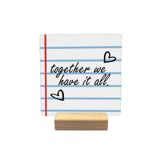 Together we have it all - Decoratie tegel - Formaat: - Op deze decoratietegel staat de tekst "together we have it all." in een zwart, cursief lettertype. De achtergrond heeft het uiterlijk van gelinieerd schriftpapier met blauwe horizontale lijnen en een rode verticale kantlijn. Het ontwerp wordt aangevuld met twee handgetekende zwarte hartjes. - Snelwenskaart