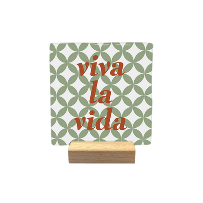 Viva la vida - Decoratie tegel - Formaat: - Op deze decoratietegel staat de tekst "viva la vida" in roodbruine, gecentreerde letters. De achtergrond is voorzien van een wit-groen geometrisch patroon van overlappende cirkels. - Snelwenskaart