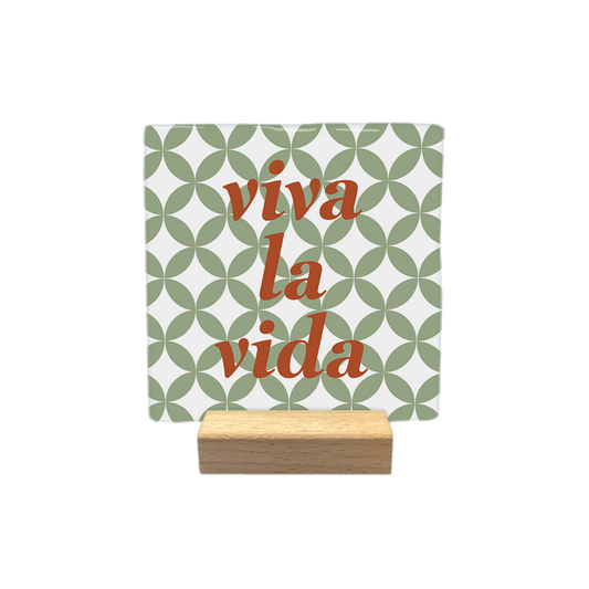 Viva la vida - Decoratie tegel - Formaat: - Op deze decoratietegel staat de tekst "viva la vida" in roodbruine, gecentreerde letters. De achtergrond is voorzien van een wit-groen geometrisch patroon van overlappende cirkels. - Snelwenskaart