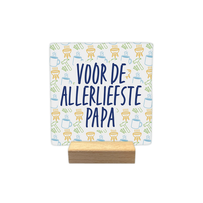 Voor de allerliefste papa - Decoratie tegel - Formaat: - Op deze decoratie tegel staat centraal in grote, donkerblauwe letters de tekst "VOOR DE ALLERLIEFSTE PAPA". De achtergrond is gevuld met een herhalend patroon van kleine, lineaire illustraties waaronder barbecues, hamers, spijkers en mokken. Deze iconen zijn uitgevoerd in verschillende kleuren, waaronder geel, lichtblauw en groen. Het ontwerp combineert een persoonlijke boodschap met een speels, thematisch patroon. - Snelwenskaart