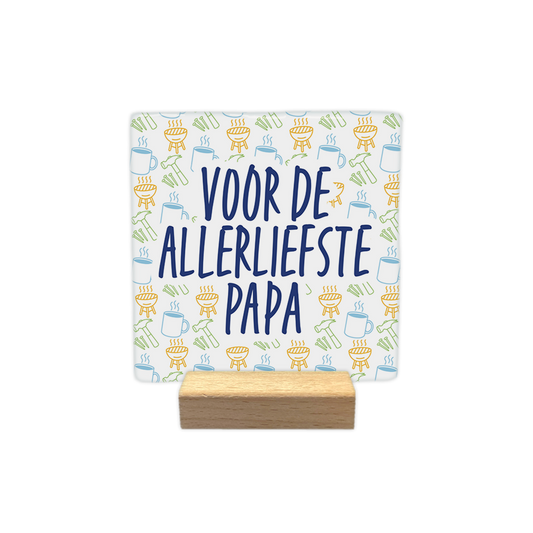 Voor de allerliefste papa - Decoratie tegel - Formaat: - Op deze decoratie tegel staat centraal in grote, donkerblauwe letters de tekst "VOOR DE ALLERLIEFSTE PAPA". De achtergrond is gevuld met een herhalend patroon van kleine, lineaire illustraties waaronder barbecues, hamers, spijkers en mokken. Deze iconen zijn uitgevoerd in verschillende kleuren, waaronder geel, lichtblauw en groen. Het ontwerp combineert een persoonlijke boodschap met een speels, thematisch patroon. - Snelwenskaart