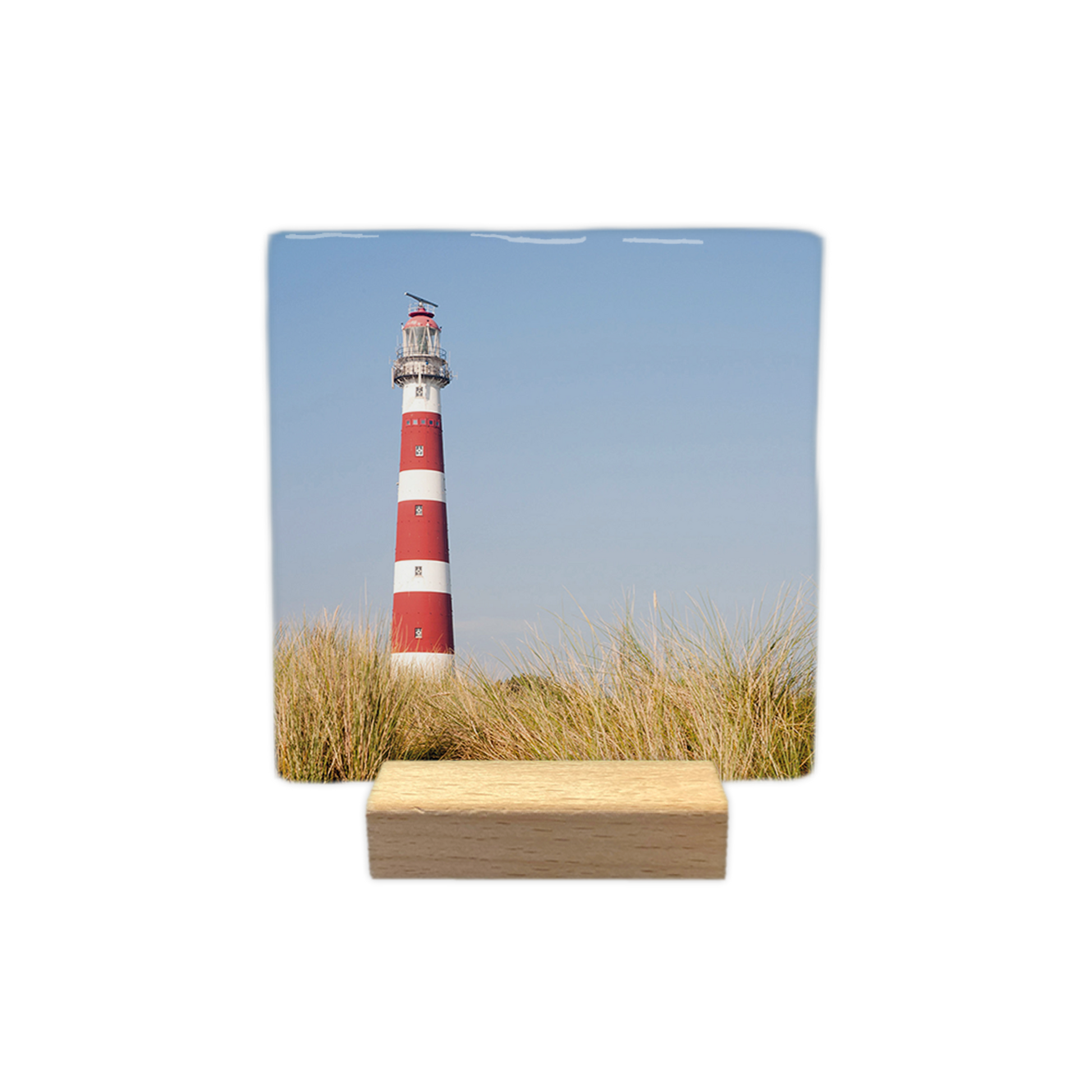 Vuurtoren Ameland - Decoratie tegel - Formaat: - Op deze decoratie tegel is een vuurtoren met rood-witte horizontale banden afgebeeld. De vuurtoren staat achter een voorgrond van duingras. De lucht op de achtergrond is helderblauw. - Snelwenskaart