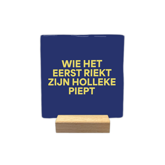 Wie het eerst riekt zien Holleke piept - Decoratie tegel - Formaat: - Op deze decoratie tegel staat de tekst "wie het eerst riekt zijn holleke piept" in vier regels afgebeeld. De tekst is geschreven in gele letters. De achtergrond van de tegel is donkerblauw. - Snelwenskaart