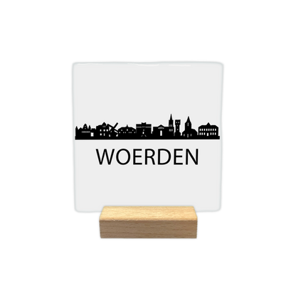 Woerden skyline - Decoratie tegel - Formaat: - Op deze decoratie tegel staat een zwarte skyline van Woerden afgebeeld tegen een witte achtergrond. In het silhouet zijn verschillende herkenbare gebouwen uit de stad te zien, waaronder een molen. Onder de skyline staat in zwarte letters de plaatsnaam Woerden. Het ontwerp is uitgevoerd in een minimalistische zwart-witstijl. - Snelwenskaart