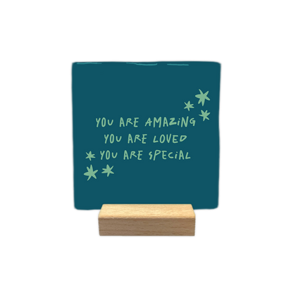 You are amazing - Decoratie tegel - Formaat: - Op deze decoratie tegel staat de tekst "you are amazing, you are loved, you are special" in lichtgroene, handgeschreven letters. Om de tekst heen zijn enkele kleine, eveneens lichtgroene sterretjes afgebeeld. Het ontwerp is geplaatst tegen een donkerblauwe achtergrond. - Snelwenskaart