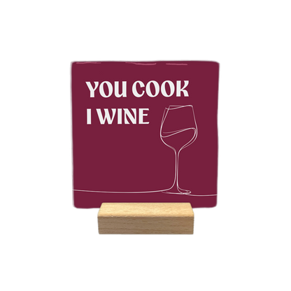 You cook I wine - Decoratie tegel - Formaat: - Op deze decoratietegel staat de tekst "YOU COOK I WINE" in witte hoofdletters. Aan de rechterkant is een minimalistische lijntekening van een wijnglas afgebeeld. De tekst en de tekening staan op een dieprode achtergrond. - Snelwenskaart