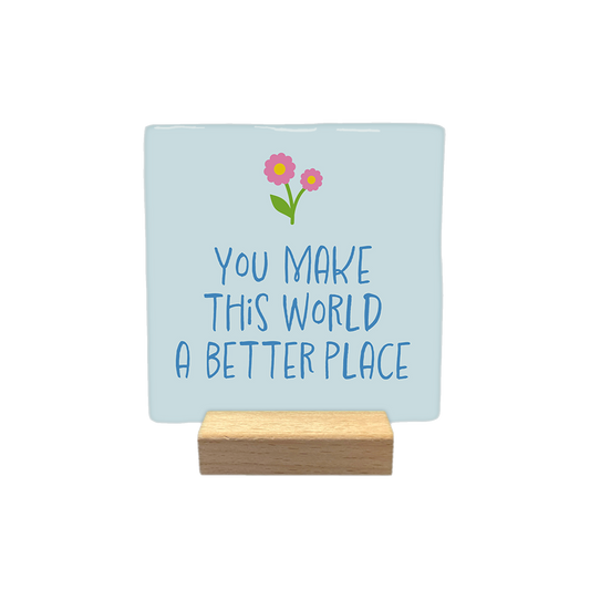 You make this world a better place - Decoratie tegel - Formaat: - Op deze decoratieteel staat de tekst 'You make this world a better place' geschreven in donderblauwe letters. Boven de tekst staan twee bloeken in de kleur roze met een gele knop en een groen blaadje. De tekst staat gecentreerd op een lichtblauwe achtergrond. - Snelwenskaart