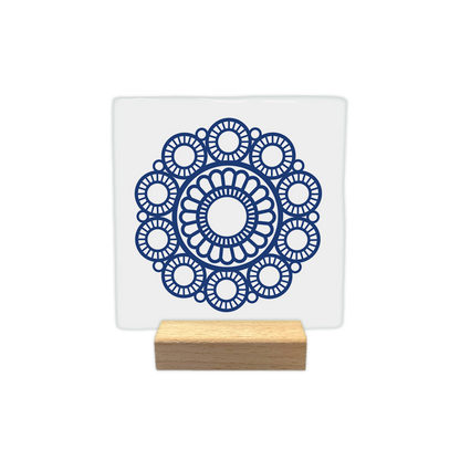 Zeeuwse knop - Decoratie tegel - Formaat: - Op deze decoratie tegel staat een blauw, symmetrisch patroon op een witte achtergrond. In het midden bevindt zich een cirkelvormig motief dat doet denken aan een bloem, omringd door een krans van kleinere, gedetailleerde cirkels. Het ontwerp heeft een decoratieve en geometrische stijl. - Snelwenskaart