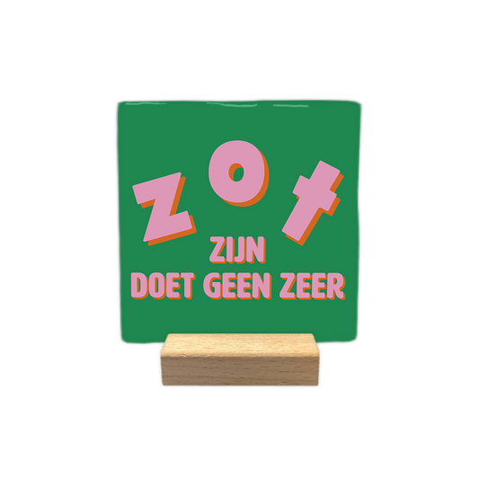 Zot zijn doet geen zeer - Decoratie tegel - Formaat: - Op deze decoratie tegel staat in het midden de tekst "zot zijn doet geen zeer". De woorden "zot" en "zijn" zijn groot en speels vormgegeven, terwijl "doet geen zeer" onderaan in een strakkere stijl staat. Alle letters zijn roze met een oranje schaduwrand. De achtergrond van de tegel is groen. - Snelwenskaart