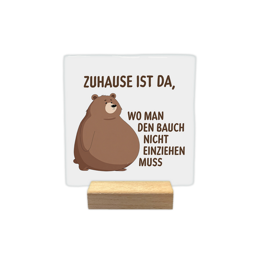 Zuhause ist da - Decoratie tegel - Formaat: - Op deze decoratie tegel staat de tekst "zuhause ist da, wo man den bauch nicht einziehen muss" in bruine letters afgebeeld. Links op de tegel is een illustratie van een bruine beer met een dikke buik te zien. De achtergrond van het ontwerp is wit. - Snelwenskaart