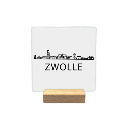 Zwolle skyline - Decoratie tegel - Formaat: - Op deze decoratie tegel staat een zwarte skyline van Zwolle afgebeeld tegen een witte achtergrond. In het silhouet zijn verschillende herkenbare gebouwen uit de stad verwerkt, waaronder een molen en diverse torens. Onder de skyline staat in zwarte letters de plaatsnaam Zwolle. Het ontwerp is uitgevoerd in een minimalistische zwart-witstijl. - Snelwenskaart
