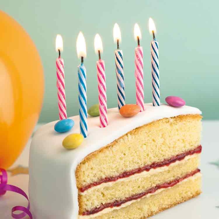 Op deze wenskaart staat een foto van een stuk taart mmet kaarsjes erop.