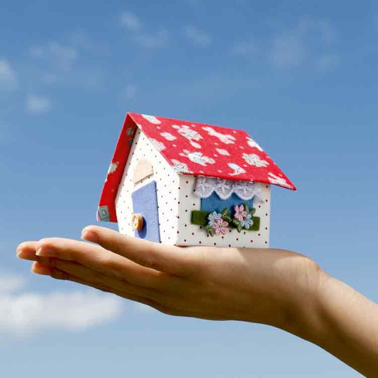 Op deze wenskaart staat een foto van een hand die een klein huisje omhoog houdt. 